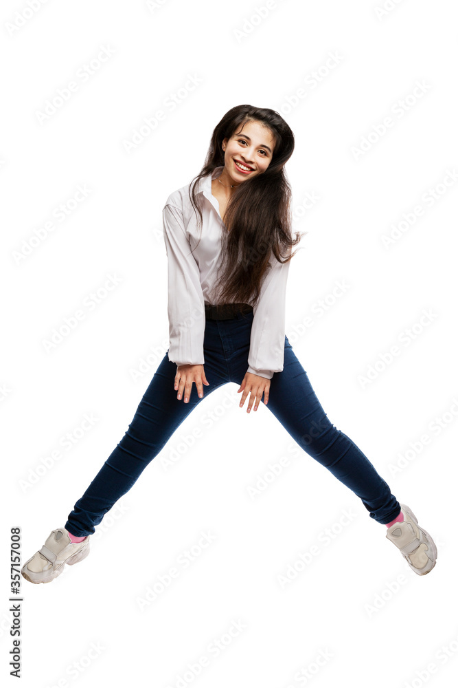 Laughing young girl with long hair is jumping. Brunette in a white shirt and jeans. Activity and energy. Isolated on a white background. Laughing young girl with long hair is jumping. Brunette in a white shirt and jeans. Activity and energy. Isolated on a white background.
