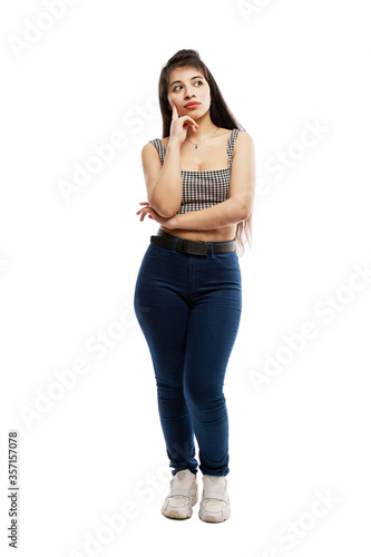 Pensive young girl in jeans. Brunette with long hair. Isolated on a white background. Vertical. Full height.