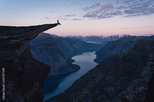A woman sitting on the edge of Trolltunga in a beautiful morning sunrise in summer season, Odda town, Norway, Scandinavia