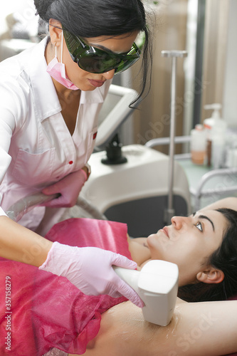 Cosmetologist making a procedure of laser epilation. Woman in beauty salon. Hair removal procedure. Body spa treatment.