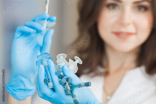 Young attractive doctor with syringe. Cosmetologist indoors making an injection. Hands holding plenty of syringes. Woman in medical parlor