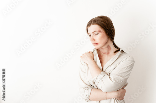 a girl sit on the den of a white stele in a shirt hugs herself from hopelessness, a victim of domestic violence, left advertising space