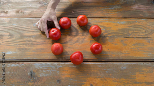 Ripe raw tomatoes on wooden table. Male hand taking one tomato. 