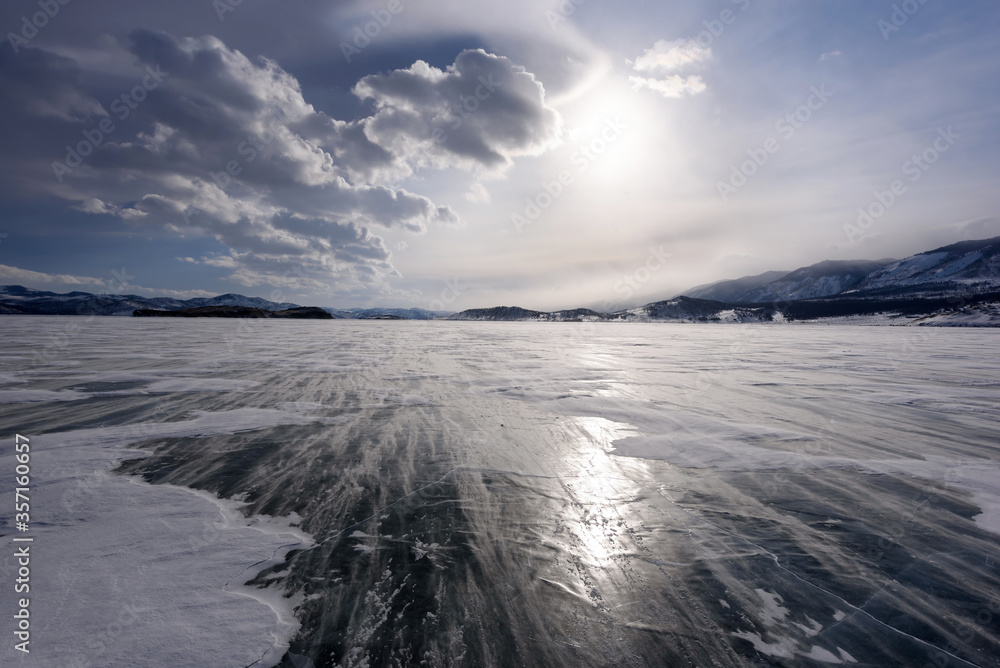 Beautiful clouds over the ice surface and windy snowdrift on a frosty day. Frozen Lake Baikal. Beautiful clouds over the ice surface and windy snowdrift on a frosty day. Frozen Lake Baikal.