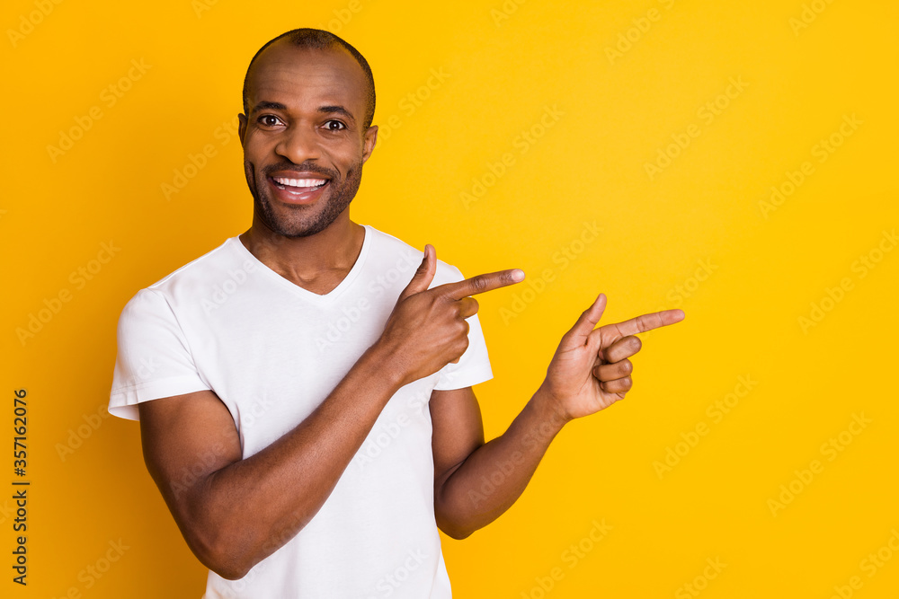 Photo of attractive dark skin guy hold arms directing fingers side empty space showing novelty information wear casual white t-shirt isolated bright vivid yellow color background Photo of attractive dark skin guy hold arms directing fingers side empty space showing novelty information wear casual white t-shirt isolated bright vivid yellow color background