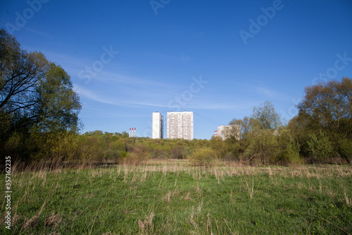 Dry grass, climbing a hill and apartment buildings, blue sky without clouds