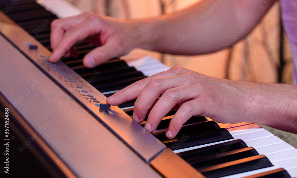 Fototapeta premium Male hands on the keys of a piano on a beautiful colored background.
