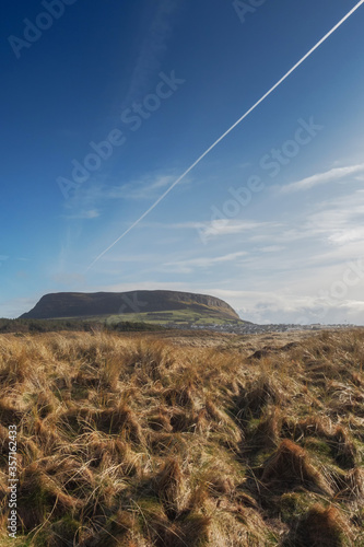 Knocknarea mountain in county Sligo, Ireland. Yellow grass and blue sky with airplane trail leading to the mountain. Strandhill town. Vertical image, nobody. photo