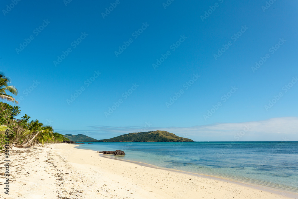 Deserted white sandy beach with palm trees and blue sky