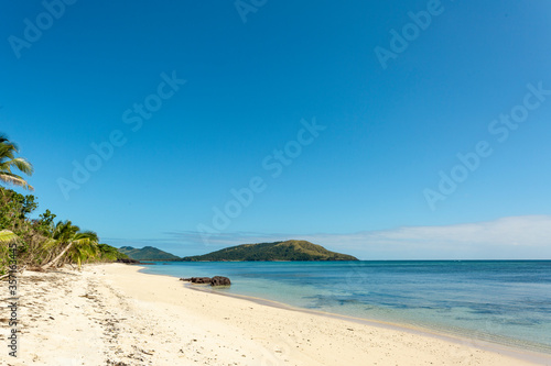 Deserted white sandy beach with palm trees and blue sky