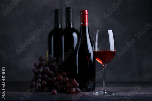 The red wine in the glass, along with a bottle of wine made from red grapes, is laid on a wooden floor and a beautiful backdrop. Ready for partying