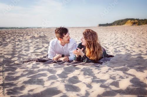 A young couple lies on the sand in clothes and talking while looking at each other. Love, trust, always be together concept