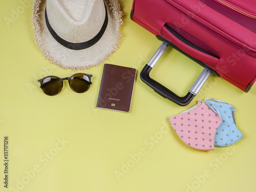 COVID-19 prevention while traveling and new normal lifestyle concept. Top view of polka dot fabric face masks with passport and travel accessories on yellow background