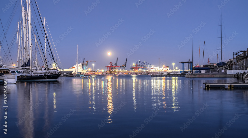 harbor docked sailboats and cargo port cranes full Moon sky and water reflection horizon night lighting