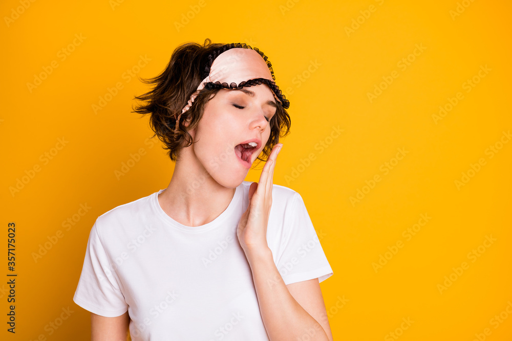 Closeup photo of pretty tired lady hold hand near open yawning mouth sleepy morning eyes closed wear night mask white t-shirt plaid pajama pants isolated yellow color background Closeup photo of pretty tired lady hold hand near open yawning mouth sleepy morning eyes closed wear night mask white t-shirt plaid pajama pants isolated yellow color background