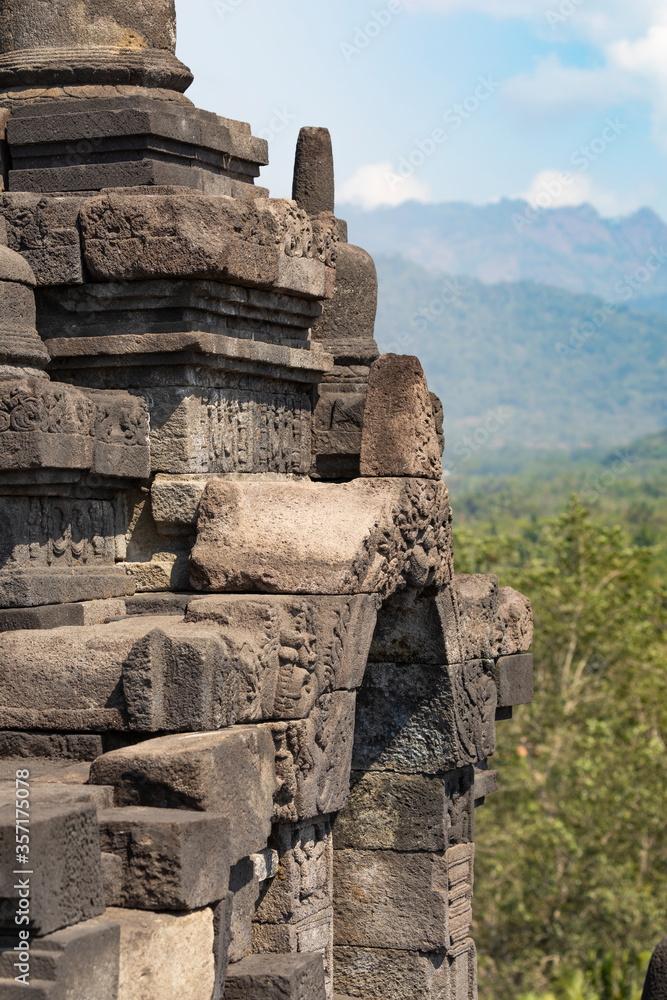 Details of various stupas that crown the balustrades and walls of the different levels of the Borobudur temple in Central Java, Indonesia, in the background, shreds of the surrounding landscape.