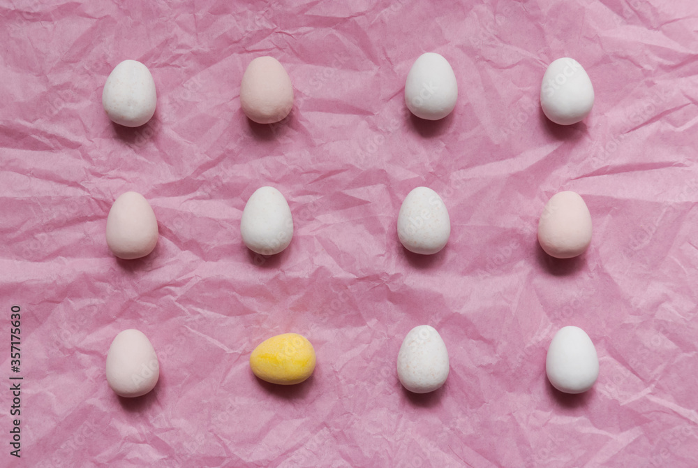 Little chocolate eggs on a pink paper background, one different yellow egg; not the same concept 