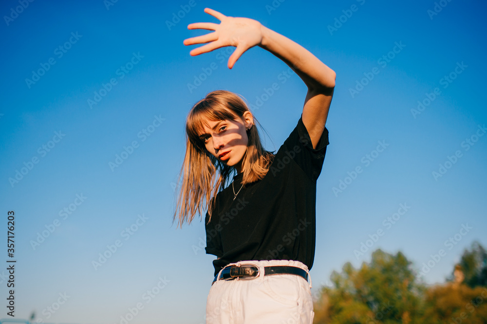 Beautiful young woman with short fair hair and blue eyes in black jacket poses for the camera on blue sky background Beautiful young woman with short fair hair and blue eyes in black jacket poses for the camera on blue sky background