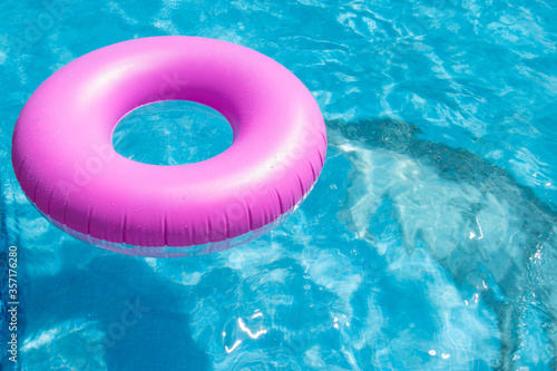 Pink rubber ring on a blue water of swimming pool, summer fun