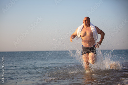 An elderly man runs along the beach. © Светлана Лазаренко