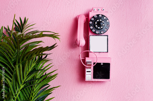 Pink old traditional phone with receiver on pastel pink background and green plant. Copy space for text