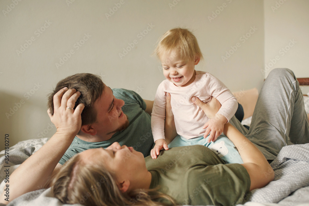 Happy family with little girl child in the morning lying in bedroom