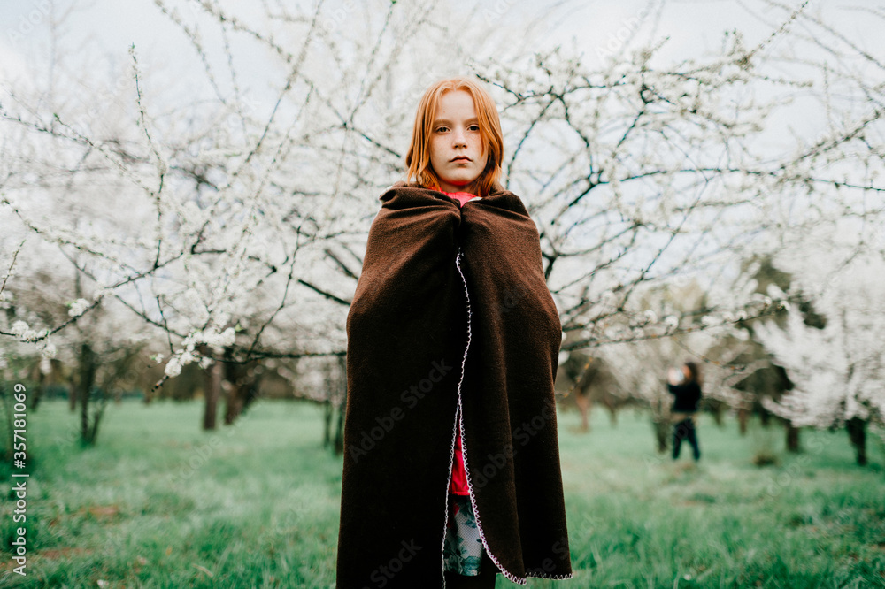 Beautiful red-haired girl wrapped herself in a warm brown plaid in a beautiful white spring garden Beautiful red-haired girl wrapped herself in a warm brown plaid in a beautiful white spring garden