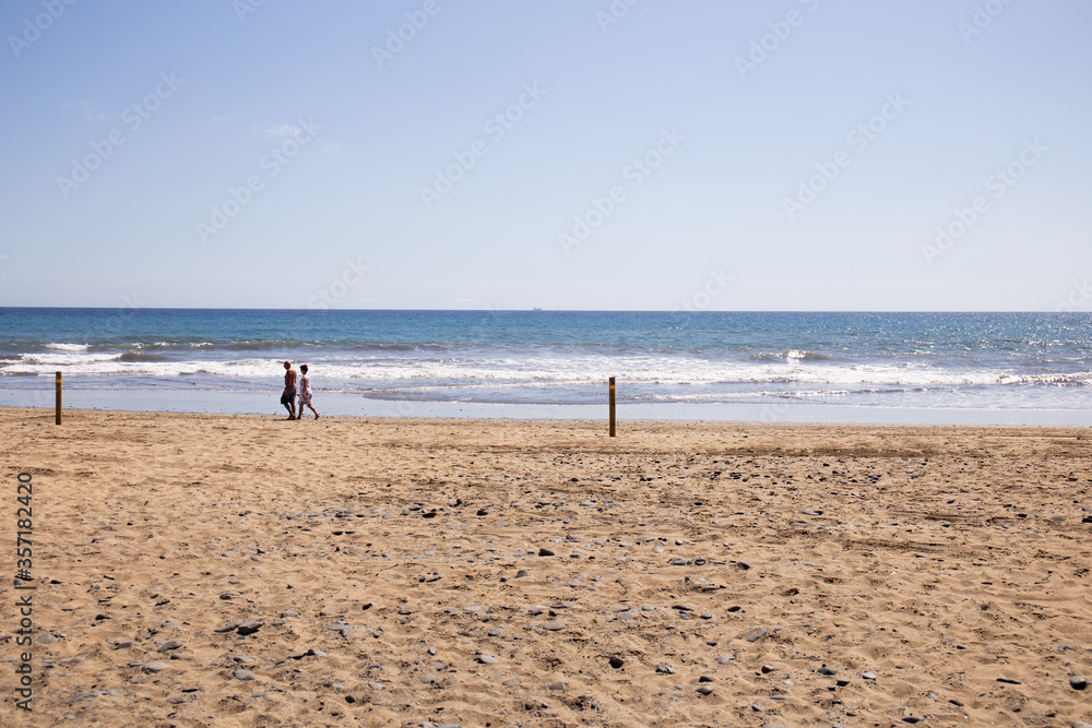 couple walking on sandy beach near Atlantic ocean at sunny day in Maspalomas, Gran Canaria