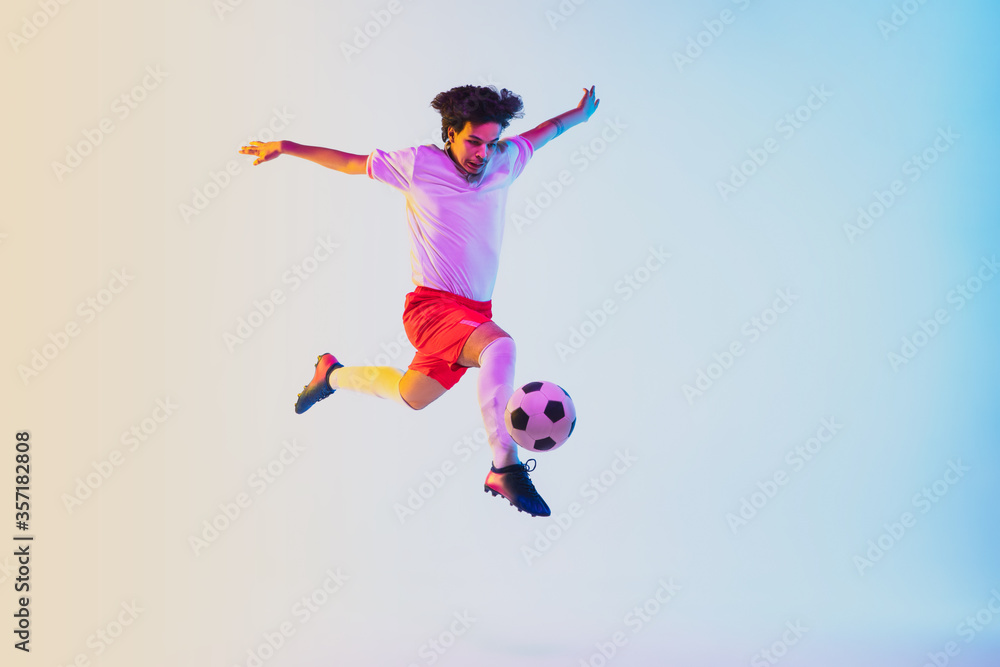Kicking in jump, on the run. Football or soccer player on gradient background in neon light - motion, action, activity. Concept of sport, competition, winning, action, motion, overcoming. Copyspace. Kicking in jump, on the run. Football or soccer player on gradient background in neon light - motion, action, activity. Concept of sport, competition, winning, action, motion, overcoming. Copyspace.
