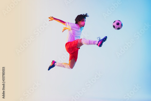 Kicking in jump, on the run. Football or soccer player on gradient background in neon light - motion, action, activity. Concept of sport, competition, winning, action, motion, overcoming. Copyspace. © master1305