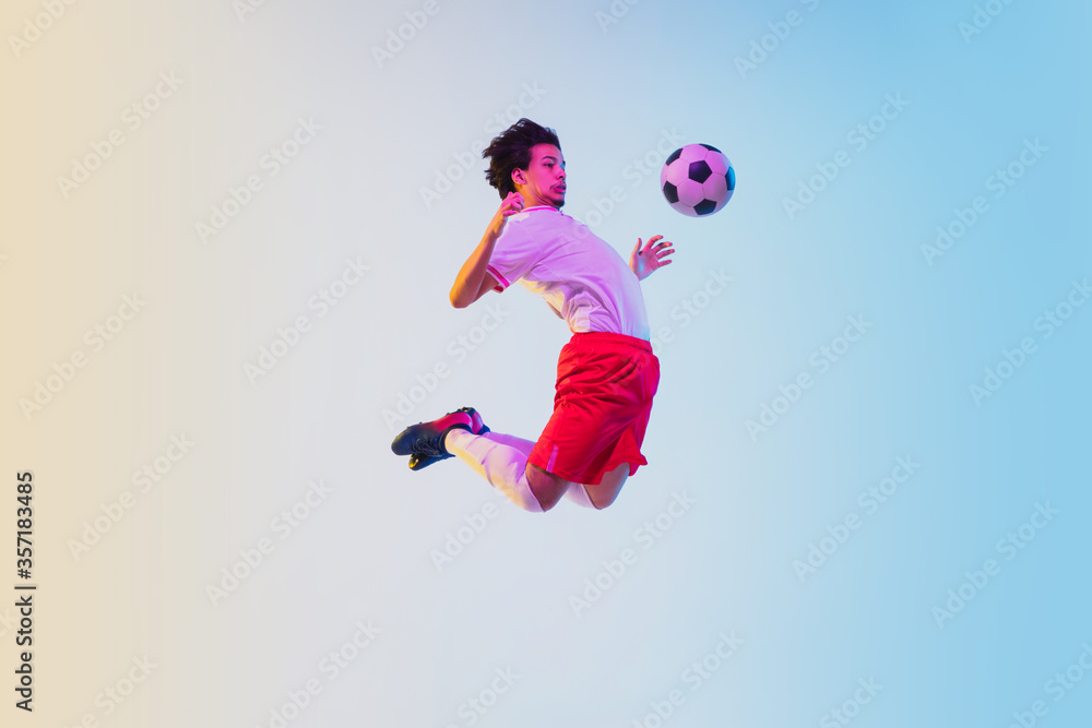 Kicking in jump, on the run. Football or soccer player on gradient background in neon light - motion, action, activity. Concept of sport, competition, winning, action, motion, overcoming. Copyspace.