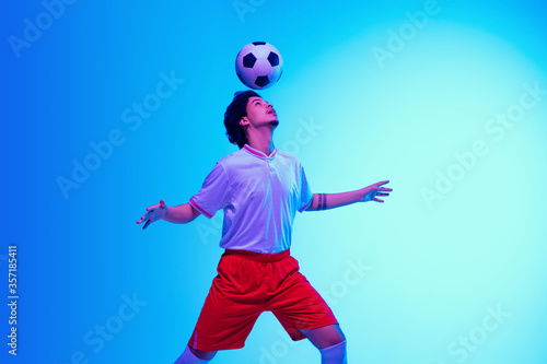 Passioned for game. Football or soccer player on gradient blue studio background in neon light - motion, action, activity. Concept of sport, competition, winning, action, motion, overcoming. Copyspace © master1305