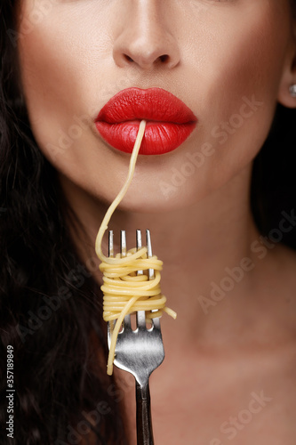 A beautiful girl eats with a fork spaghetti with red lips.