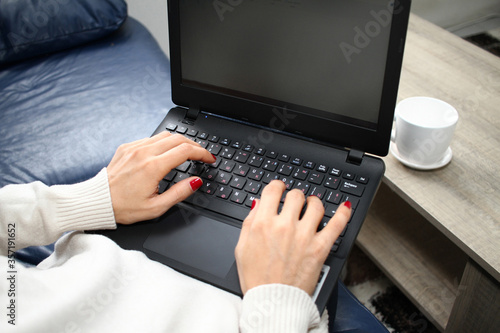 Woman hands with red nails is typing on keyboard on a laptop with coffee mug in front of her.