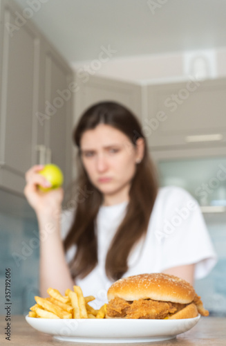 Vegan woman eats an apple against the backdrop of unhealthy fast food. Choosing the right food