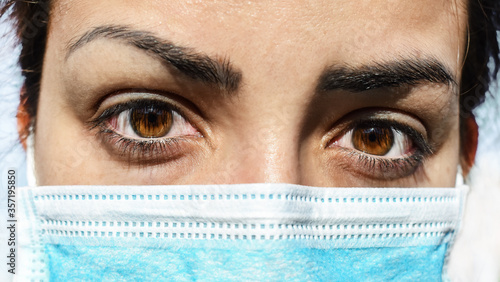 Tired gaze of female carer, nurse or doctor, wearing a surgical face mask, during a break. Overworked healthcare professional