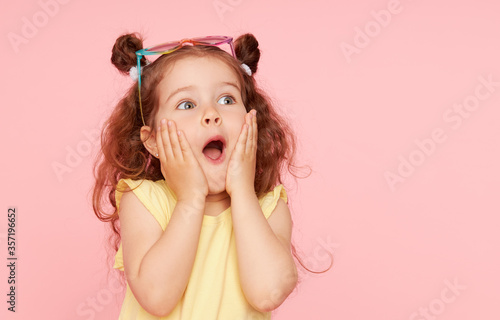 Portrait of surprised cute little toddler girl  in sunglasses over pink background.  Child model have fun and jump. Advertising childrens products