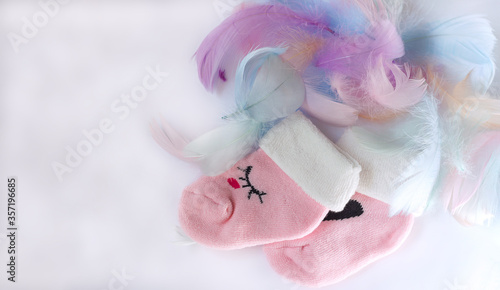 Pink children's socks and colored feathers on a white background, tenderness lightness and convenience of children's goods
