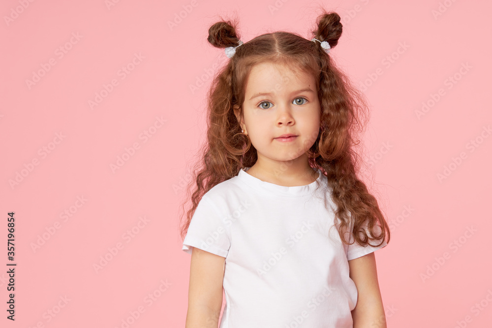 Portrait of cute european little toddler girl over pink background. Looking at camera. Child model in white T-shirt. Advertising childrens products Portrait of cute european little toddler girl over pink background. Looking at camera. Child model in white T-shirt. Advertising childrens products