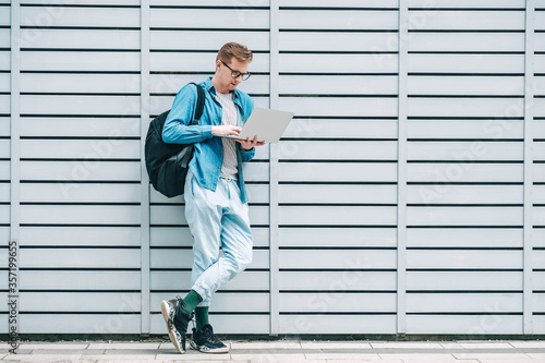 Young handsome man in shirt  jeans and glasses carrying a backpack using laptop computer standing on a wooden panel background. Freelance work concept. Copy  empty space for text
