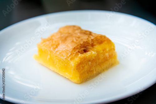 Delicious Greek sweet pastry named Galaktoboureko, made of semolina custard in filo, served with honey in white plate.