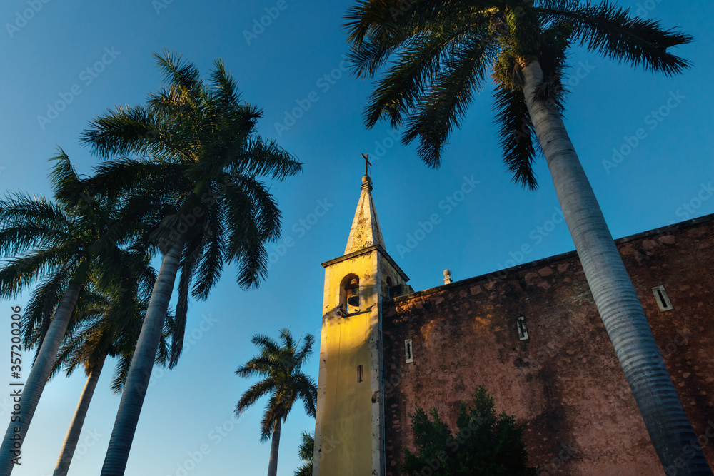 Bell tower of Santa Ana church framed by palm trees during sunset light, Merida, Yucatan, Mexico