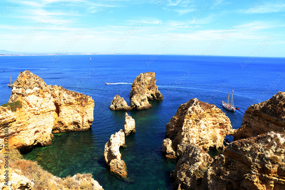 Cliff rocks and tourist boat on sea at Lagos, Algarve region, Portugal
