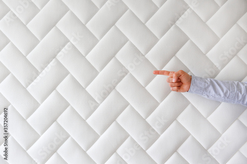 Cropped shot of man's hand pointing at copy space over white orthopedic mattress pattern. Hypoallergenic foam matress w/ proper spinal alingment & pressure point relief features. Background, close up. photo