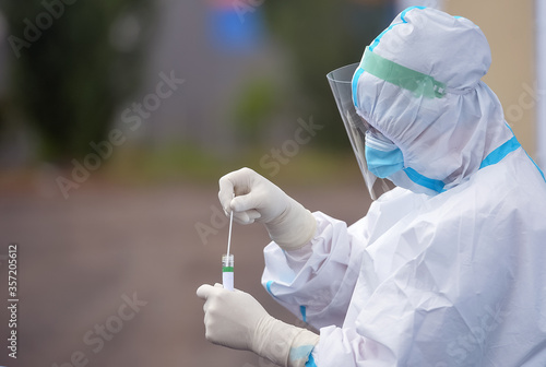 Unrecognizable people wearing protective suit handles a pharyngeal exudate/ swab collection kit for the coronavirus. Test tube for taking OP NP patient specimen sample, PCR DNA testing