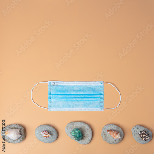 On an orange background, a medical mask, pebbles and shells. Concept protect yourself from coronovirus