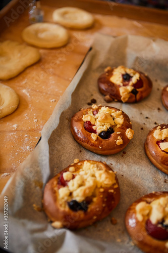 golden, homemade buns with fruit and crumble on white baking paper. in the background buns ready for baking in the oven.