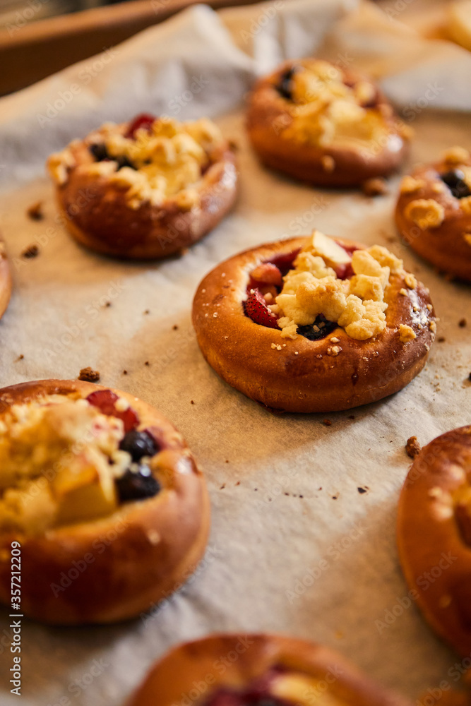 Freshly baked buns with fruits and crumble on white baking paper.