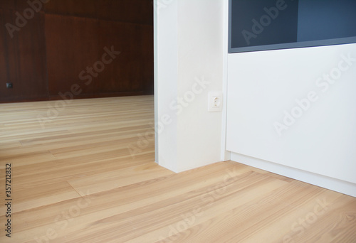 A close-up on electrical socket, outlet installed near the doorway close to wood laminated flooring, at low height of a floor.