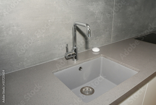 Photos A close-up on undermount enameled cast iron single basin gray kitchen sink with a stainless steel kitchen faucet against gray wall